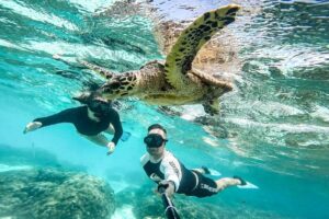 two divers take a selfie with a turtle underwater