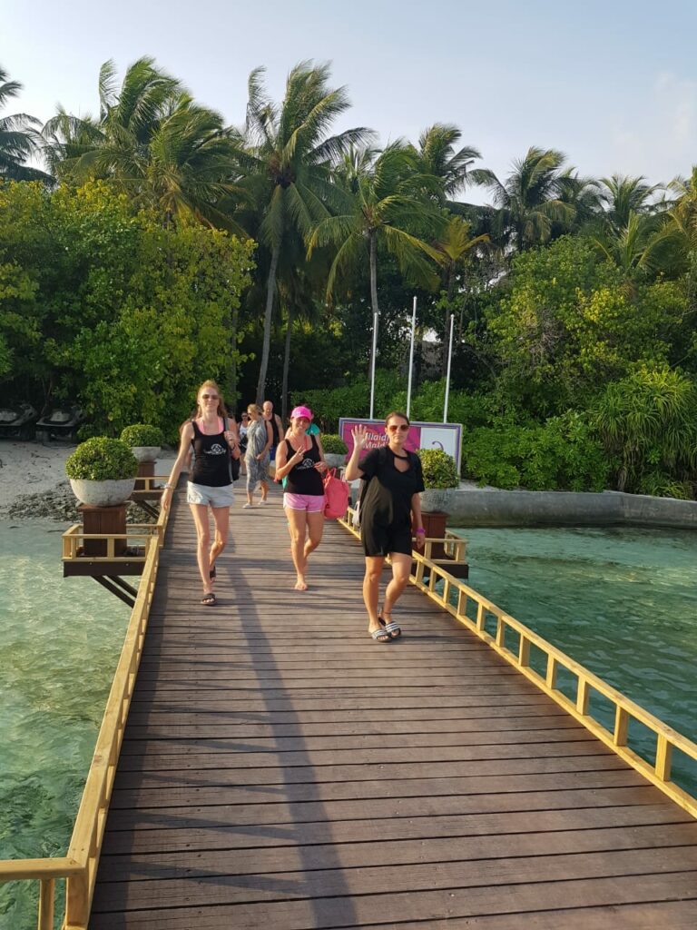 People on a wooden footbridge to the sea with palm trees in the background