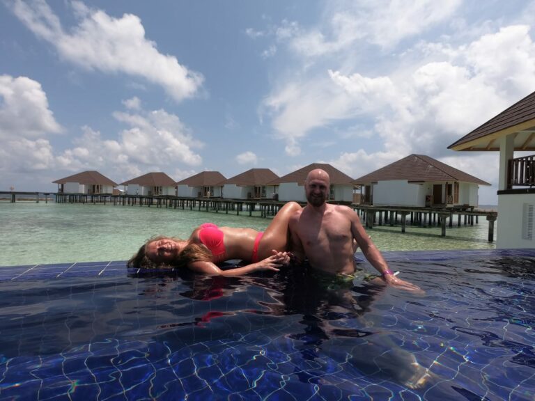 Man and woman in swimsuits in a pool overlooking cabanas with accommodation on stilts