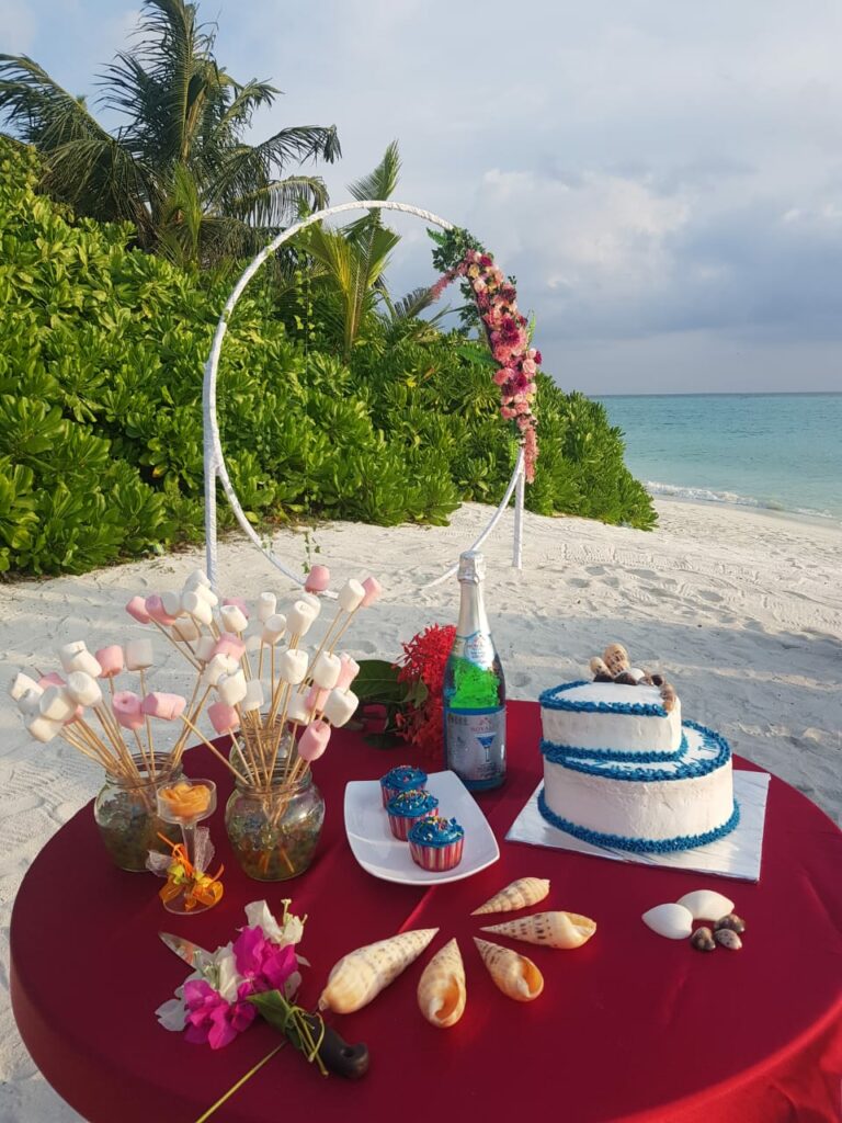 Wedding table with cake and champagne on a sandy beach with greenery and the sea in the background