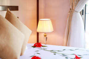 Two pillows and flowers on the bed with a lighted lamp in the background