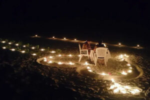 romantic dinner on the sandy beach among the candles forming a heart